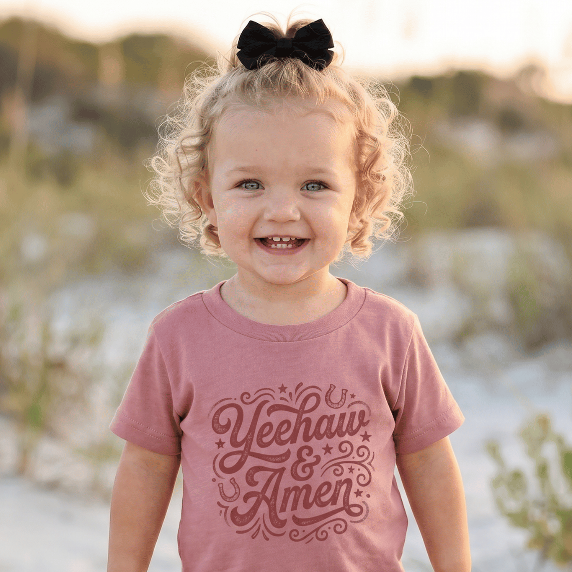 Child wearing a pink shirt with text and cow print pants standing on a sandy beach.